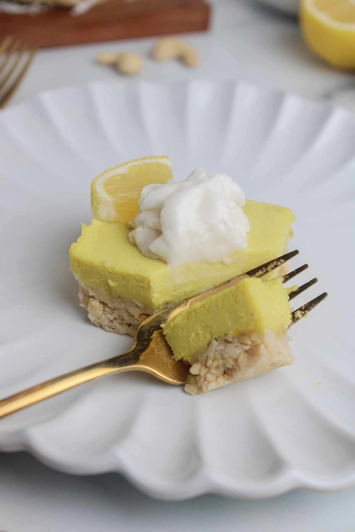 Close-up of a bright yellow vegan lemon cheesecake square on a white plate, with a fork taking a bite.