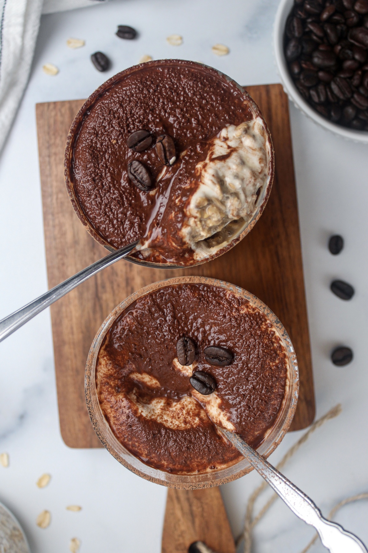 Top-down view of two glasses of tiramisu-inspired overnight oats, each with a spoon.