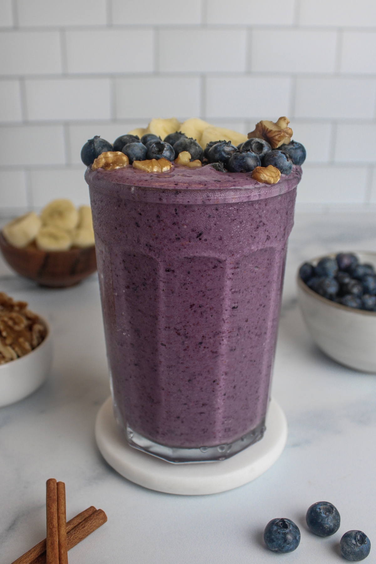 A vibrant purple blueberry banana walnut smoothie in a glass, topped with banana slices, blueberries, and walnuts.