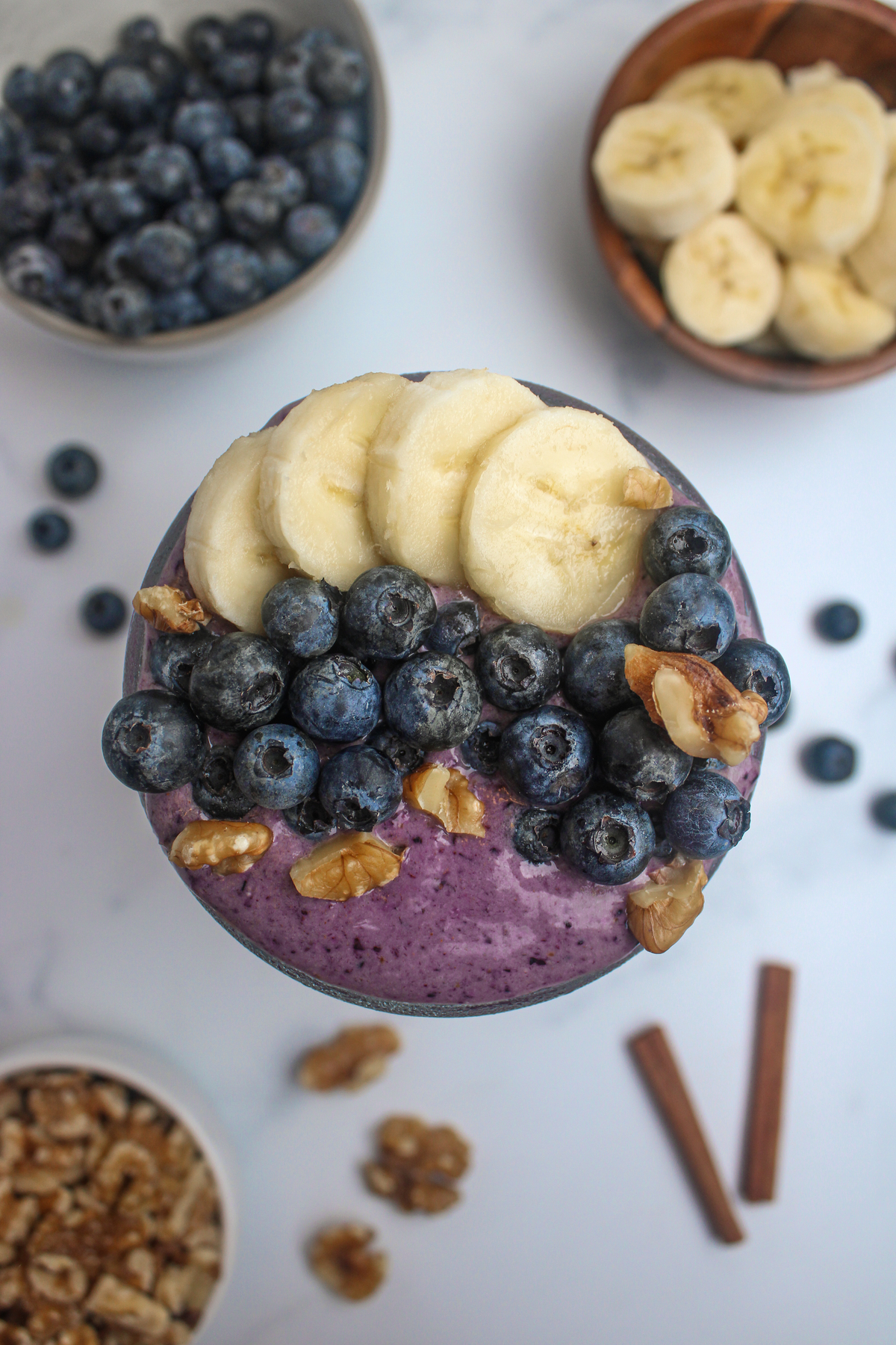 Overhead close-up of a blueberry smoothie topped with banana slices, blueberries, and walnuts.