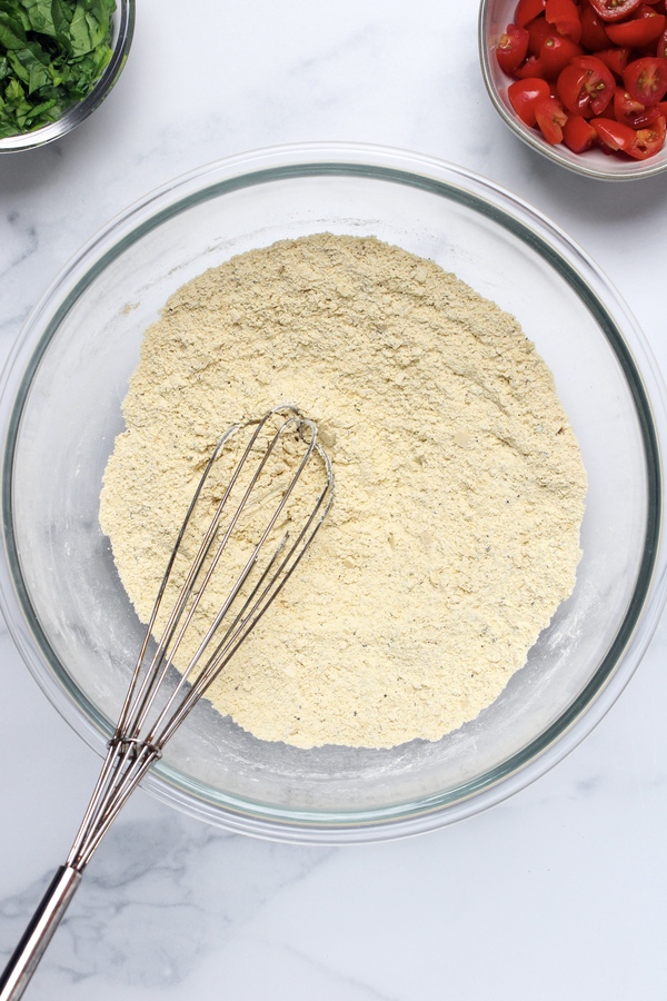 Chickpea flour, nutritional yeast, salt, pepper, baking powder, and seasonings whisked together in a bowl.