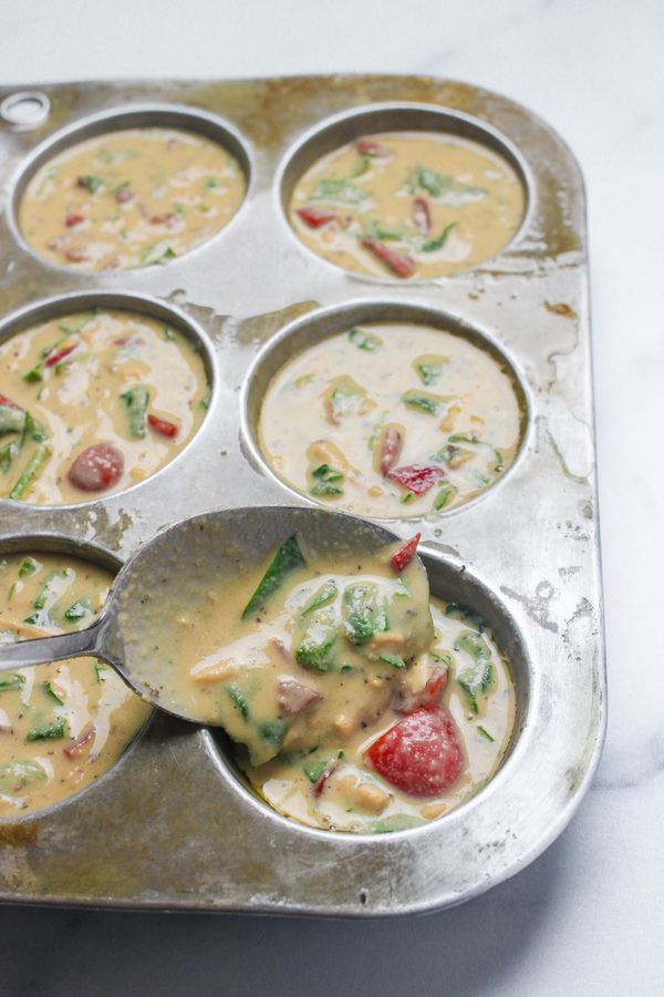 Scooping chickpea flour muffin batter into a muffin tin.
