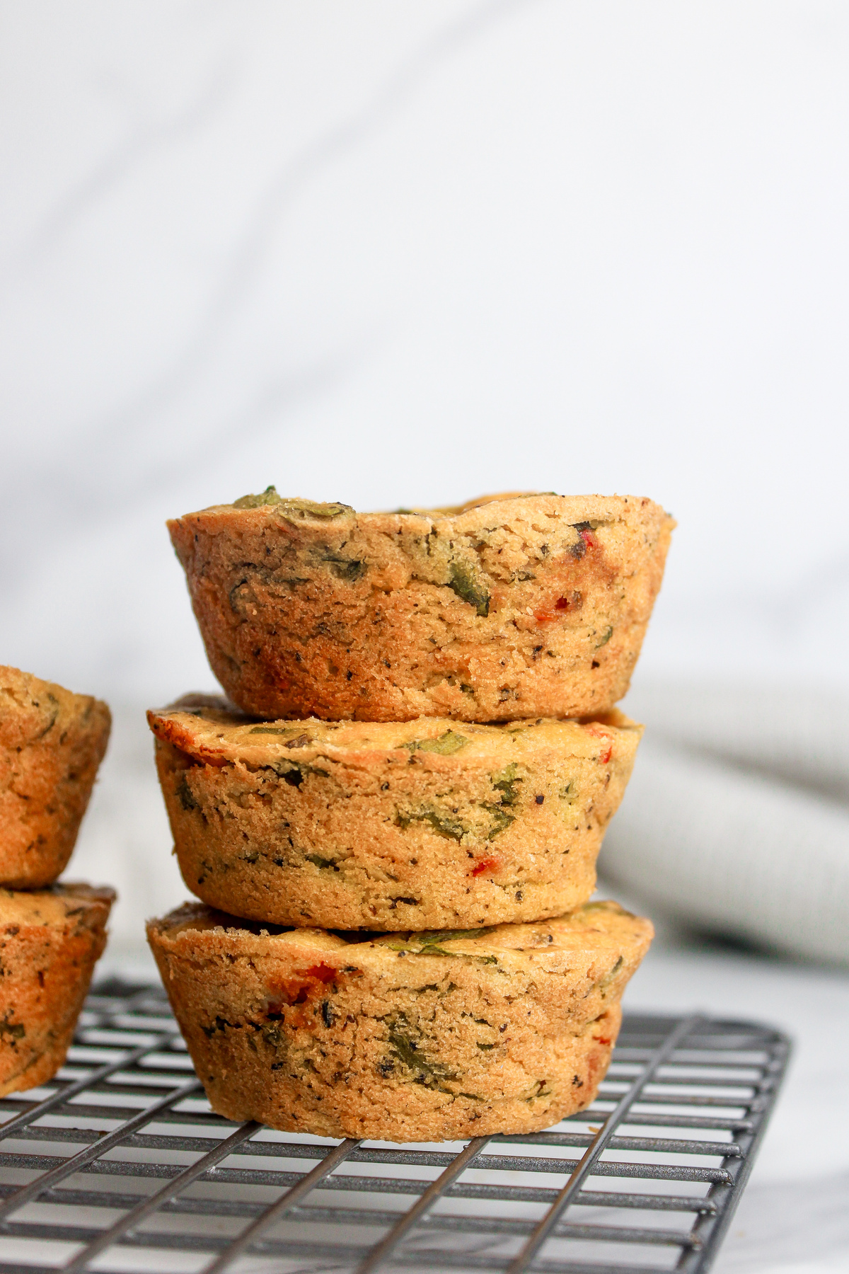 Straight-on closeup of three stacked savory chickpea flour muffins, showing red and green flecks of vegetables inside.
