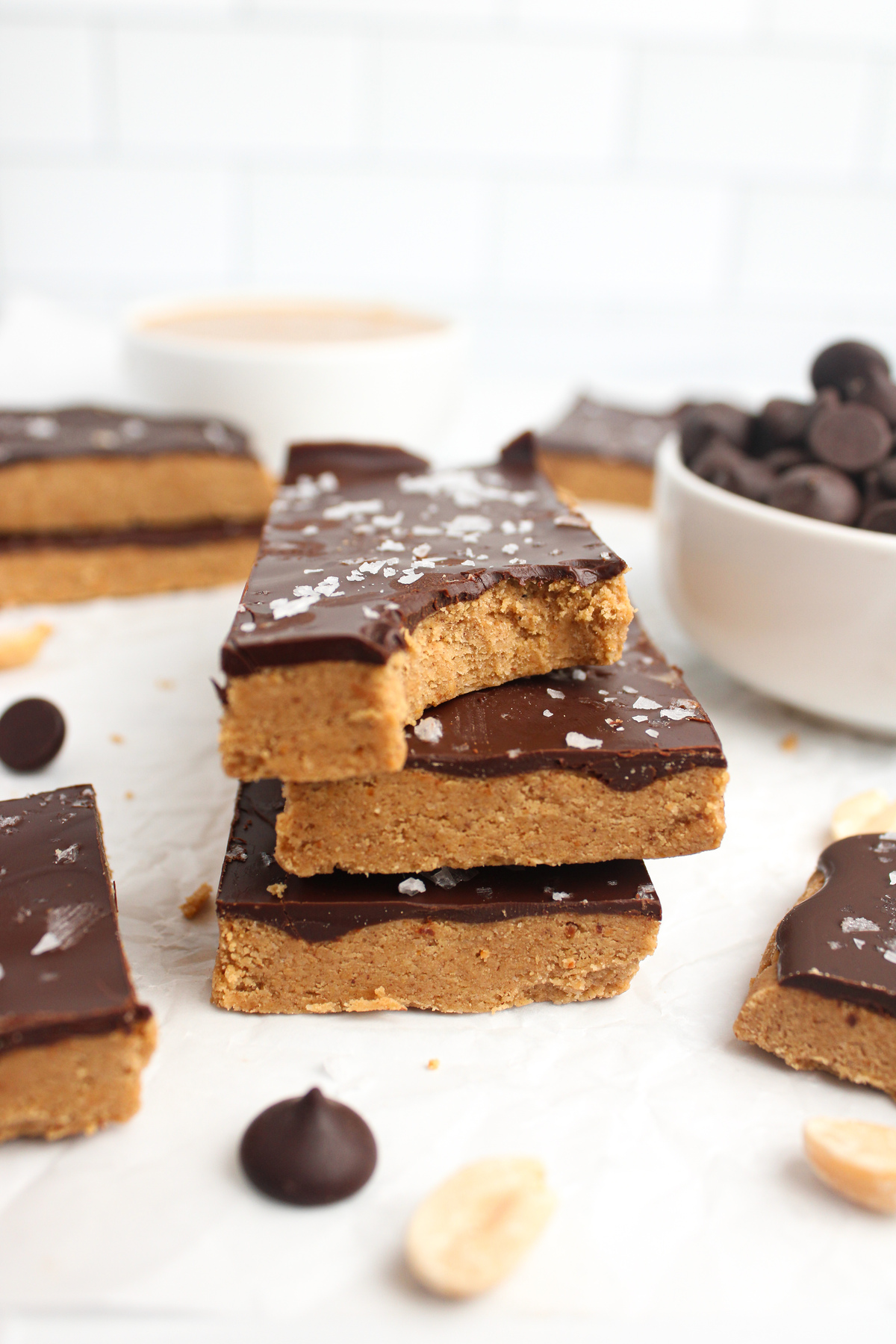 Stack of three chocolate peanut butter protein bars topped with flaky sea salt, with a bite taken out of one.