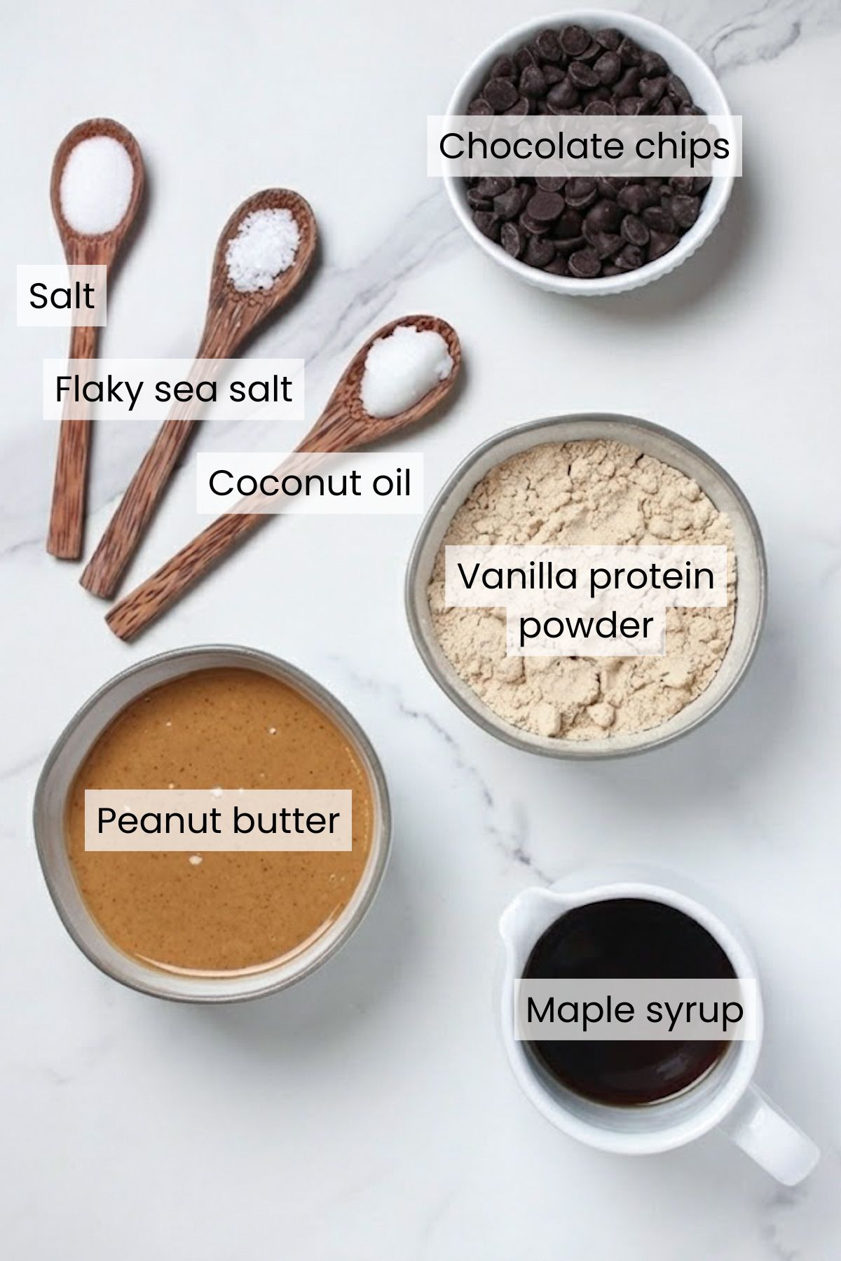 Ingredients for chocolate peanut butter protein bars: chocolate chips, salt, flaky sea salt, coconut oil, vanilla protein powder, peanut butter, and maple syrup.