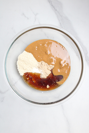 Peanut butter, protein powder, maple syrup, and salt in a bowl, ready to be mixed together.