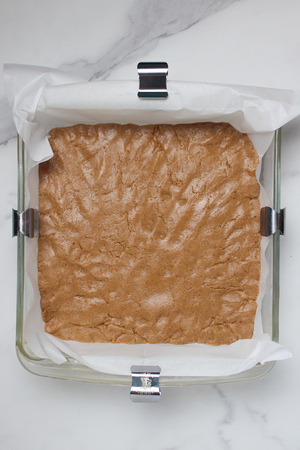 Protein bar mixture pressed evenly into a parchment-lined pan.