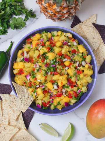 Overhead view of mango pineapple salsa in a bowl, with a tortilla chip dipping into it.