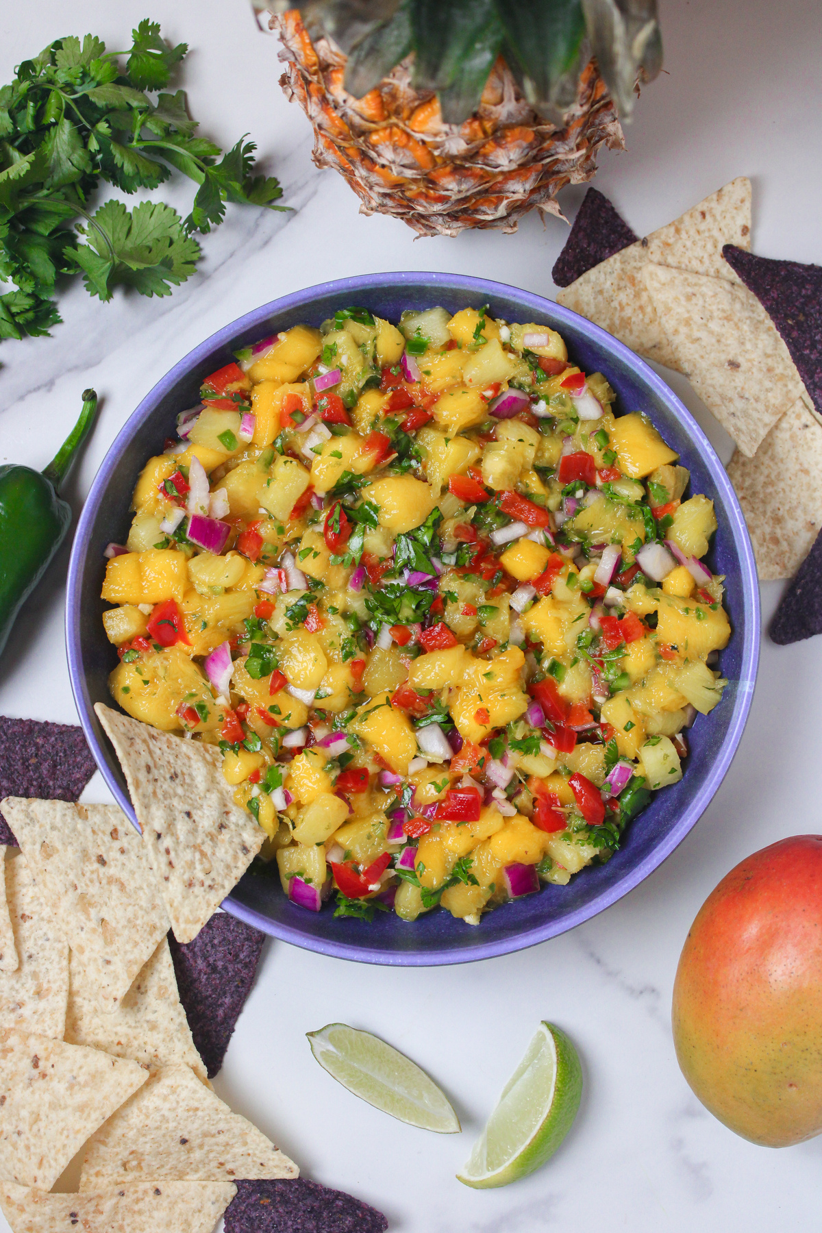 Overhead view of mango pineapple salsa in a bowl, with a tortilla chip dipping into it.