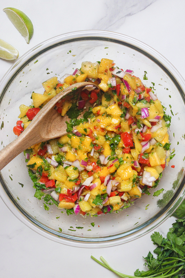 Mango pineapple salsa mixed together in a bowl with a wooden spoon.