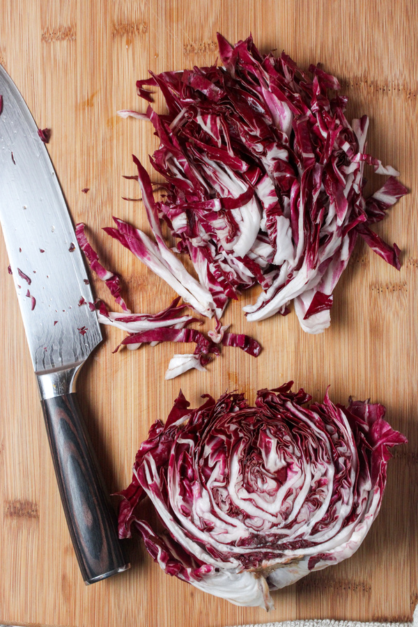 Vibrant purple radicchio leaves cut into thin strips on a wooden cutting board beside a large knife.