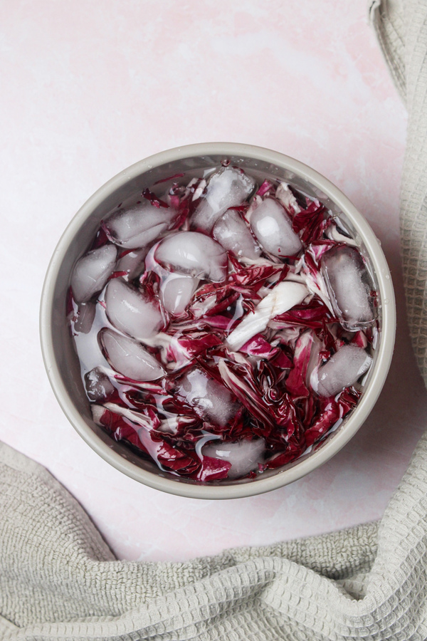 Radicchio leaves soaking in a bowl of water with ice cubes.