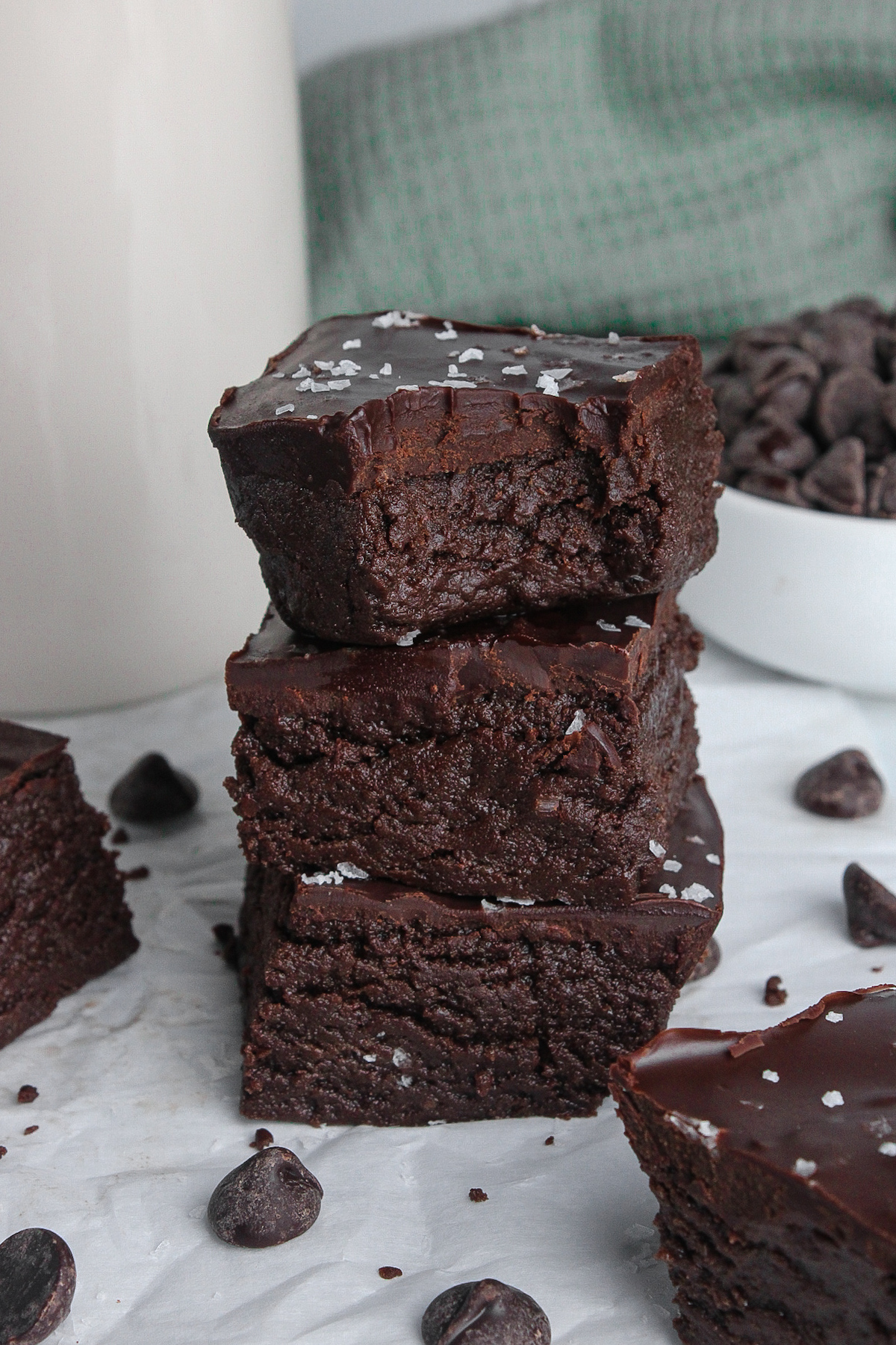 Stack of three vegan protein brownies, with a bite taken out of one to reveal the rich chocolate ganache.
