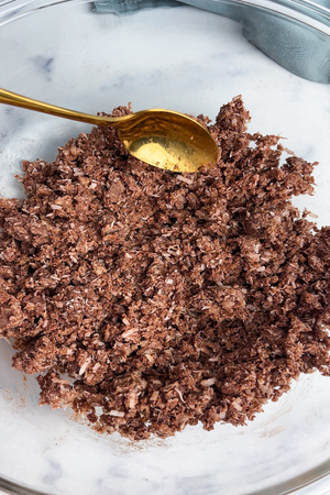 Desiccated coconut, almond flour, protein powder, melted coconut oil, and maple syrup mixed together in a bowl.