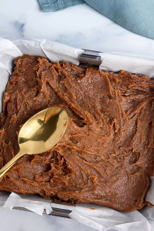 Using a spoon to spread the date caramel in an even layer over the crust.