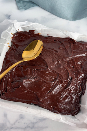 Spreading melted chocolate over the caramel layer with a spoon.