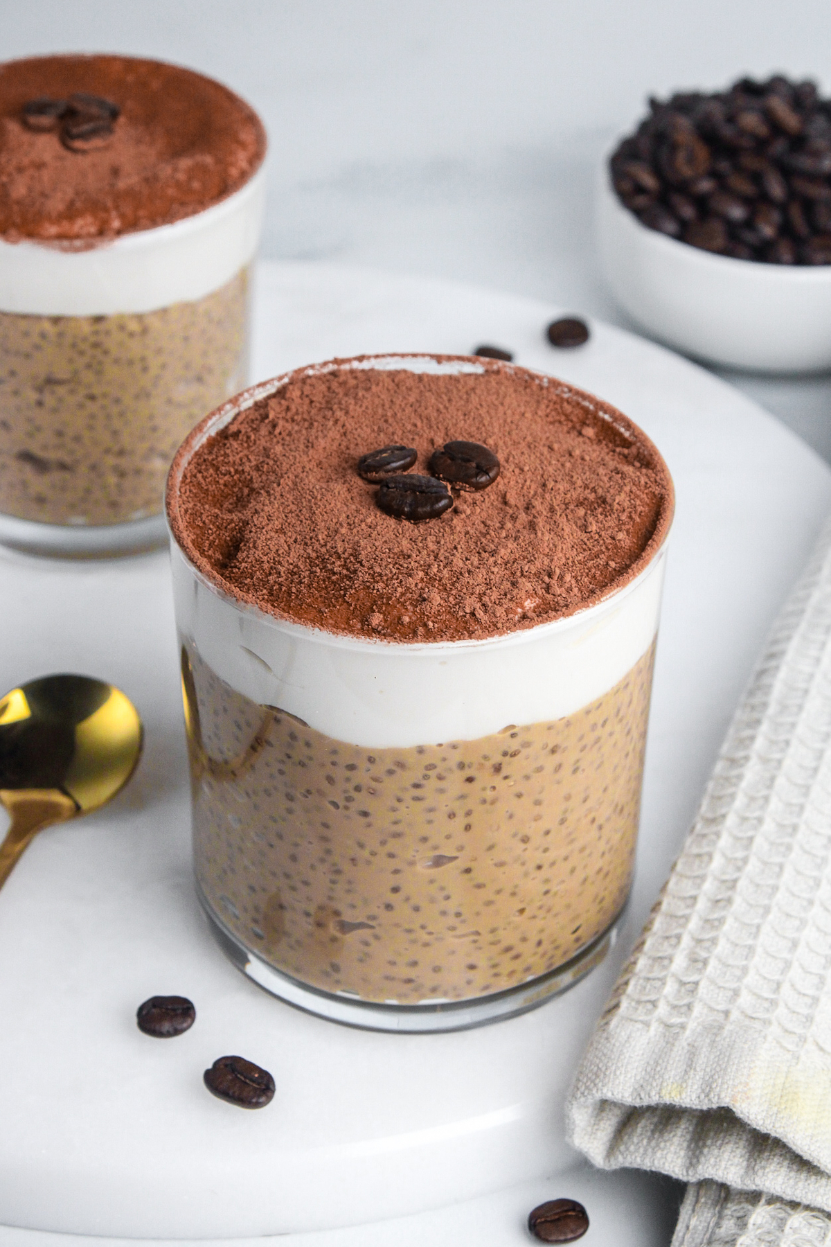 Tiramisu chia pudding in a glass, with layers of coffee-flavored chia pudding, yogurt, and cocoa powder on top.