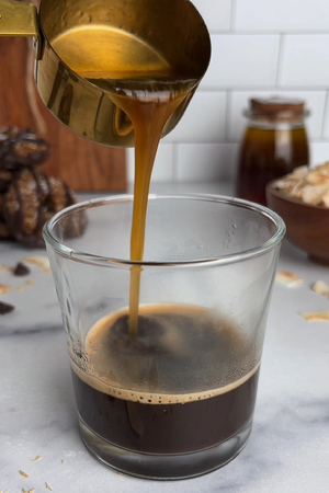 Pouring caramel syrup into a glass of freshly brewed espresso.