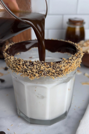 Glass rimmed with chocolate syrup and toasted coconut, filled with ice, coconut milk, and caramel-sweetened espresso.