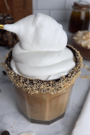 Dollop of coconut whipped cream being spooned onto the iced latte.