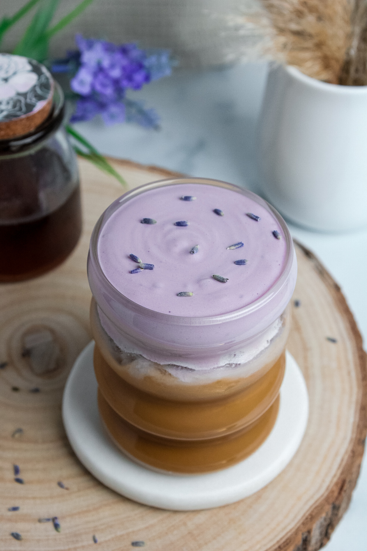 Angled view of an iced lavender cream latte showing vibrant purple cold foam and dried lavender buds on top.