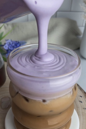 Lavender cold foam being poured over an iced latte.