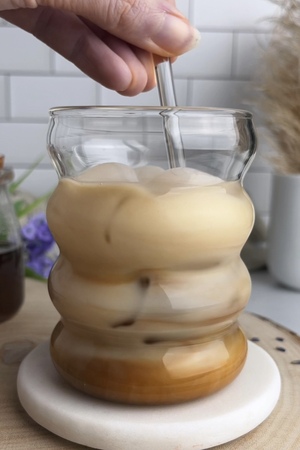Ice, oat milk, and espresso being stirred together in a glass.