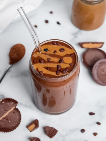Peanut butter cup smoothie in a glass with a straw, topped with a peanut butter drizzle and cacao nibs.