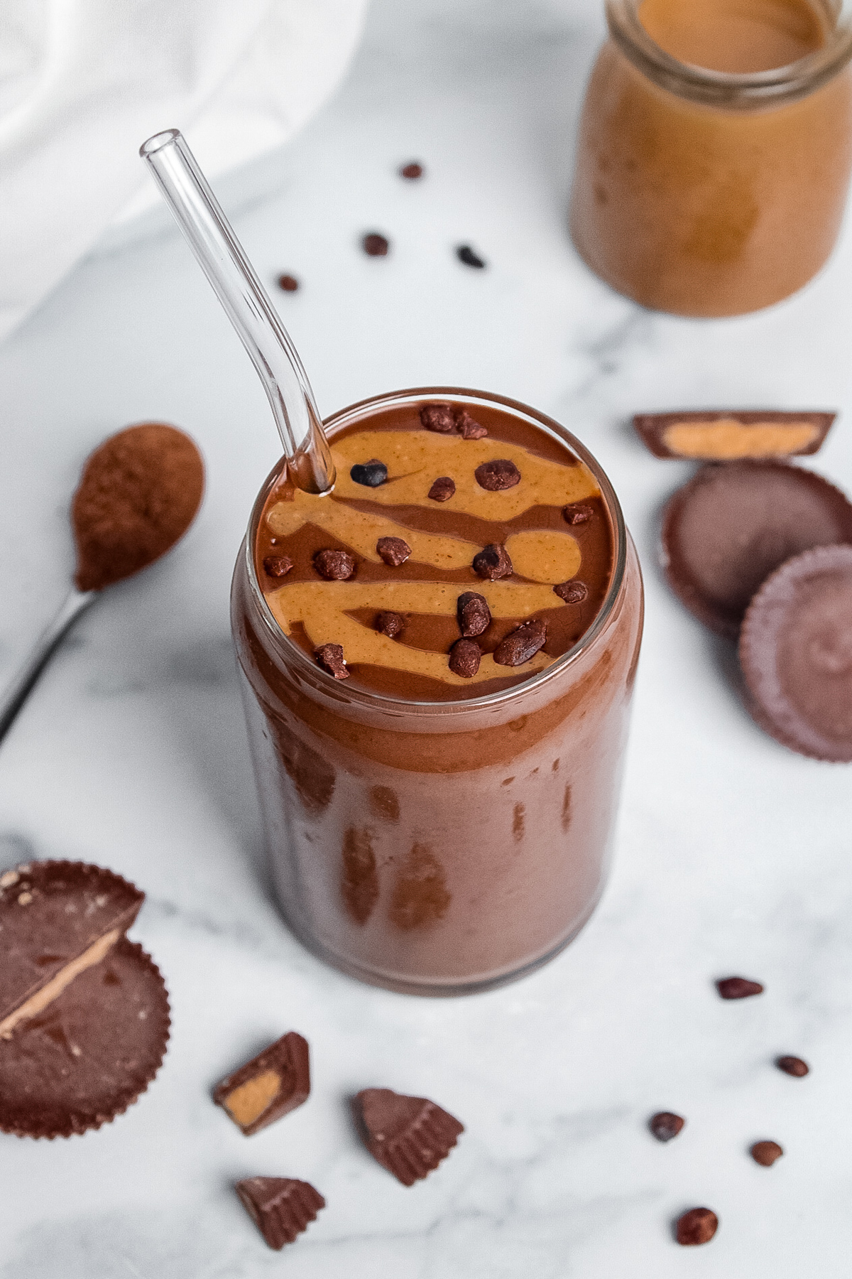 Peanut butter cup smoothie in a glass with a straw, topped with a peanut butter drizzle and cacao nibs.