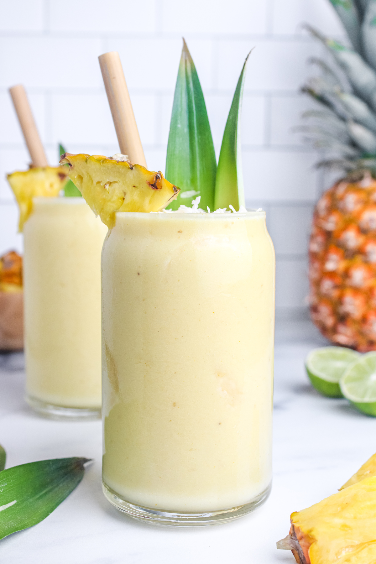 Creamy piña colada mocktail in a glass, garnished with fresh pineapple and coconut, with a bamboo straw.