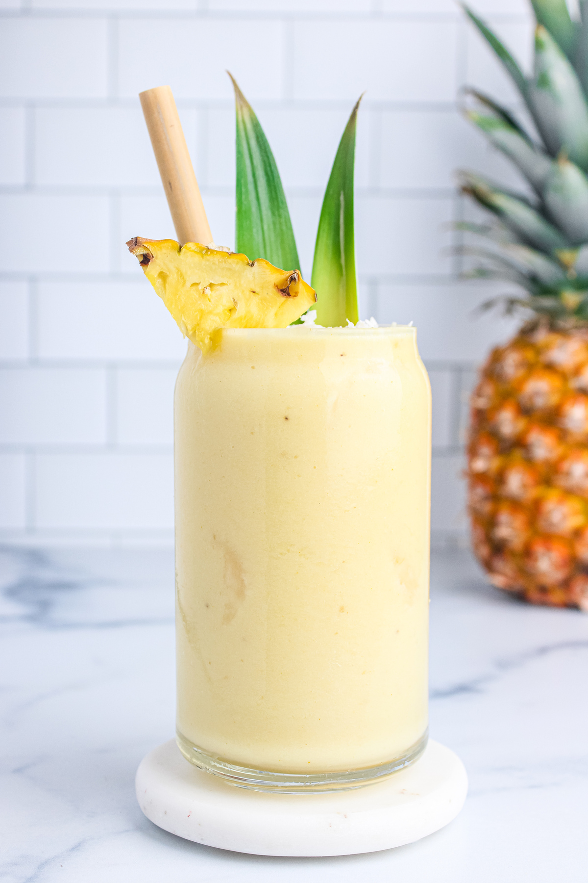 Front view of a piña colada mocktail in a glass with a bamboo straw, garnished with pineapple and shredded coconut.