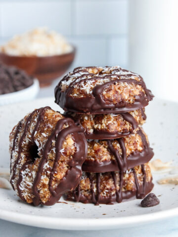 Stack of healthy no-bake Samoa cookies made with dates and toasted coconut, drizzled with chocolate, on a plate.