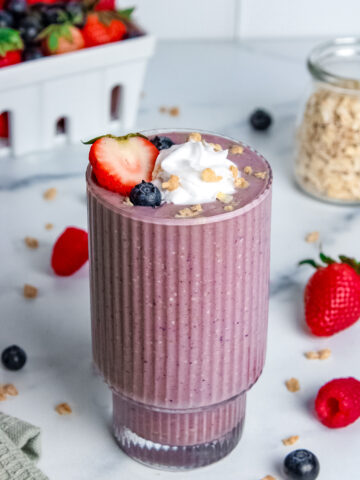 Berry pie smoothie in a glass, topped with whipped cream, granola, and fresh berries.