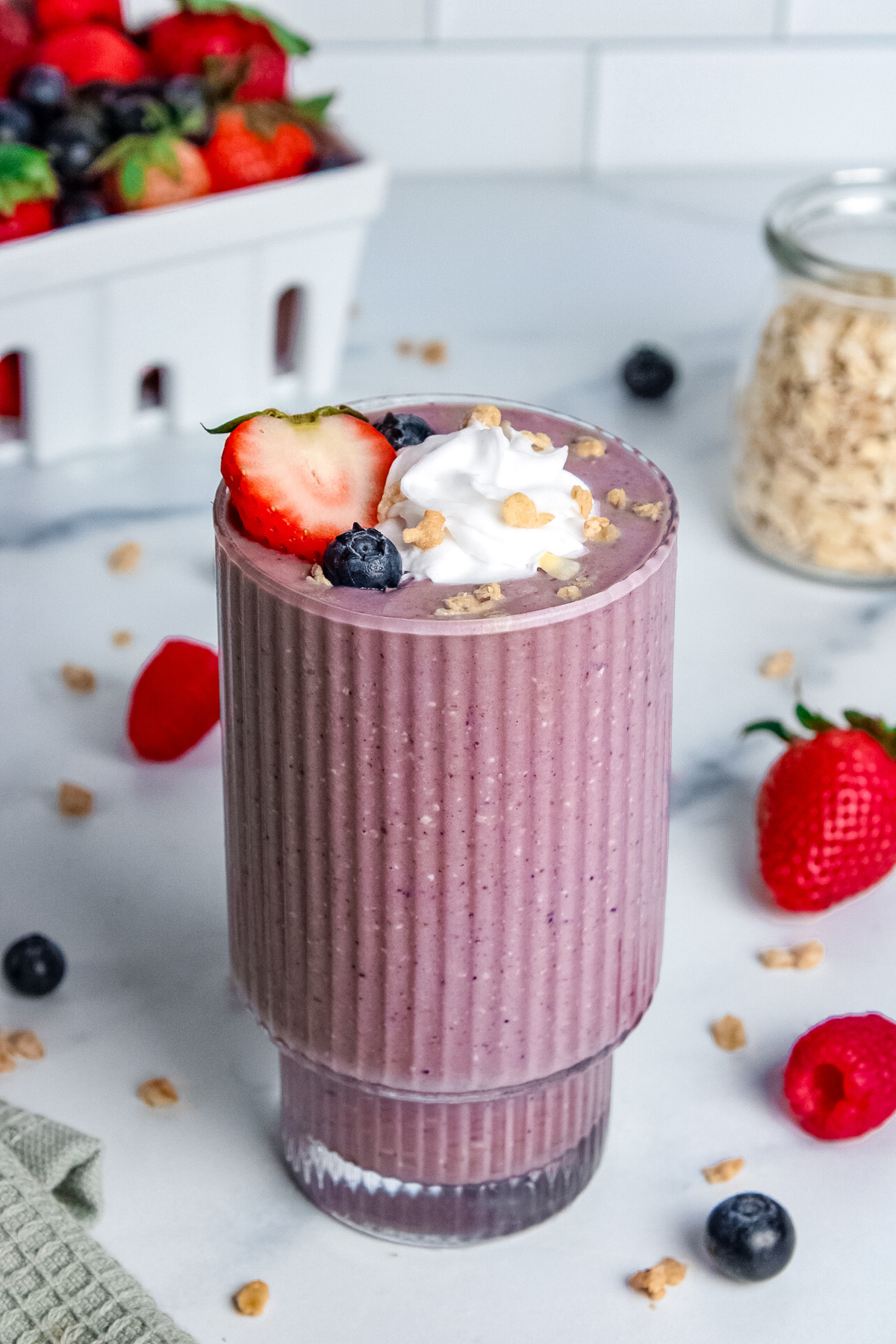 Berry pie smoothie in a glass, topped with whipped cream, granola, and fresh berries.