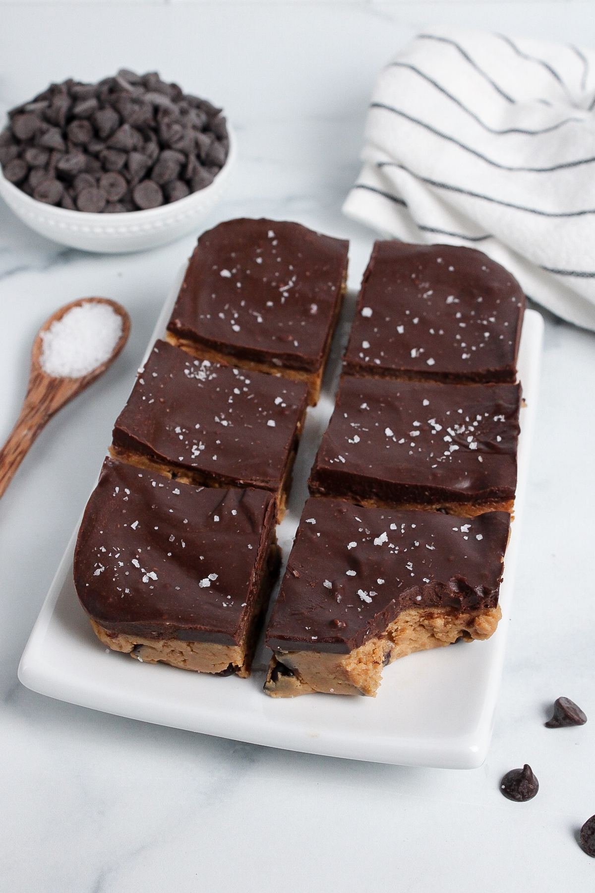 Batch of vegan no-bake cookie dough bars on a plate, topped with rich chocolate ganache and flaky sea salt.