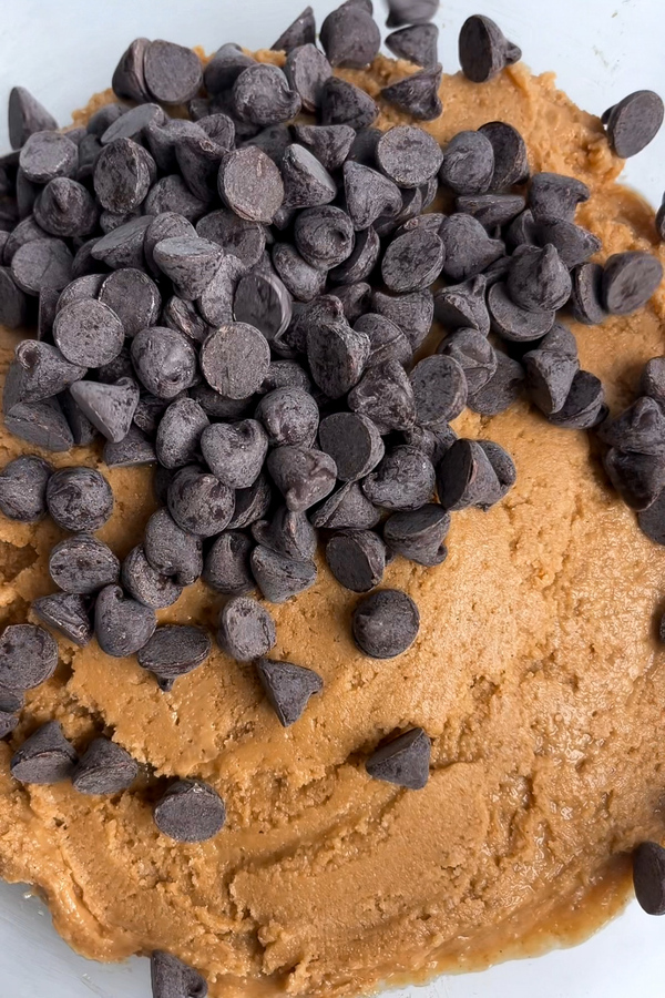 No-bake cookie dough in a bowl with chocolate chips added, ready to be folded in.