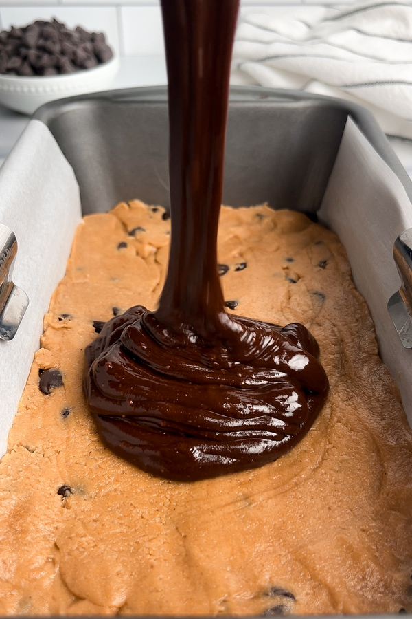 Pouring thick chocolate ganache over the cookie dough layer.