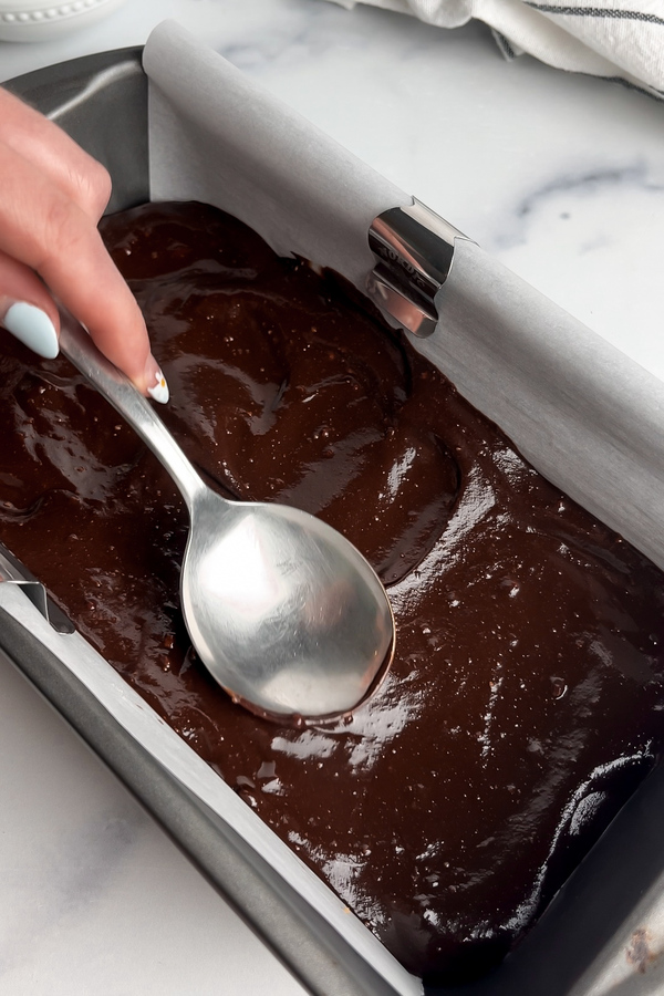 Spreading chocolate ganache over no-bake cookie dough with a spoon.