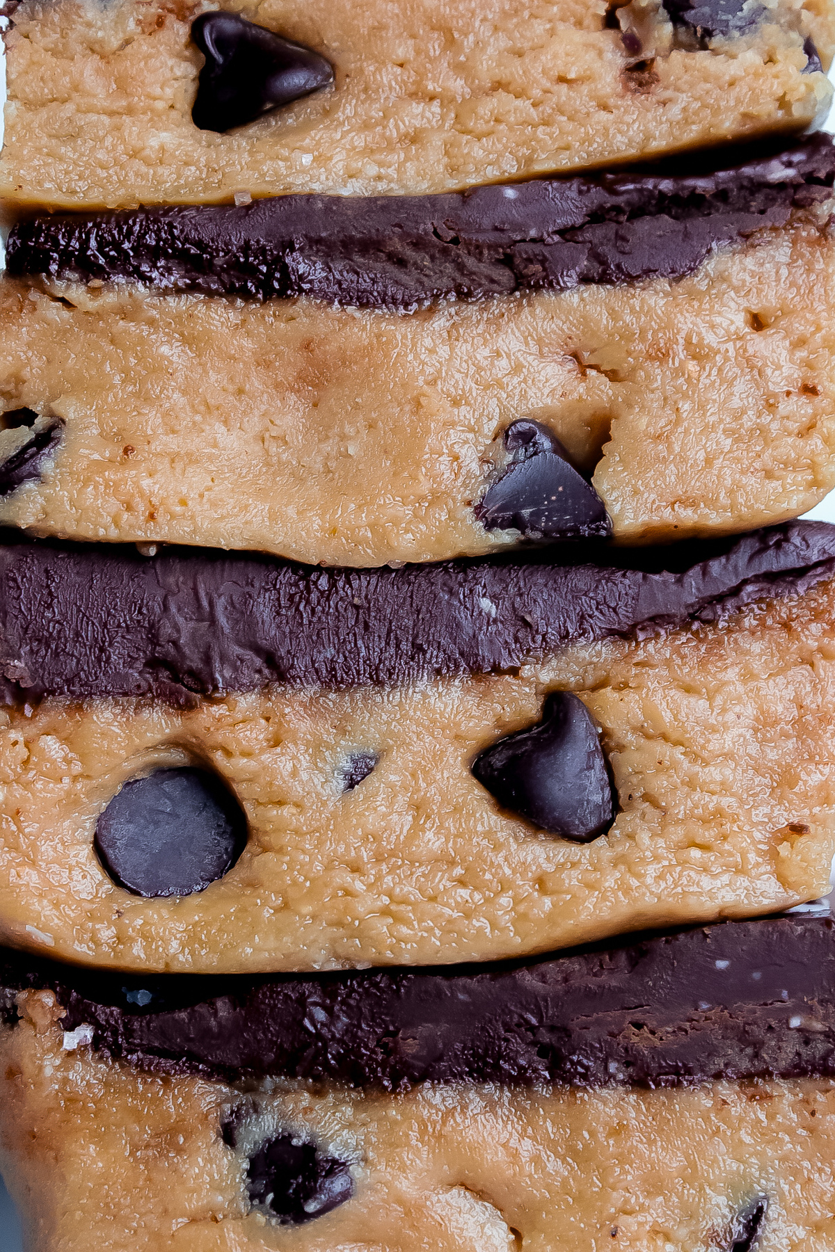 Straight-on close-up of no-bake cookie dough bars, highlighting the rich texture, silky ganache, and chocolate chips inside.