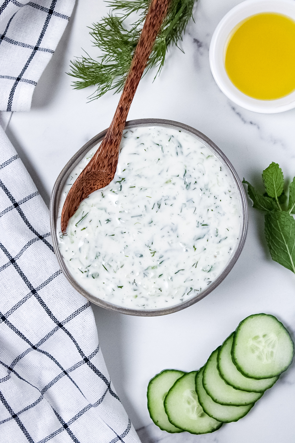 Creamy homemade dairy-free tzatziki in a small bowl with a spoon, with flecks of fresh dill.