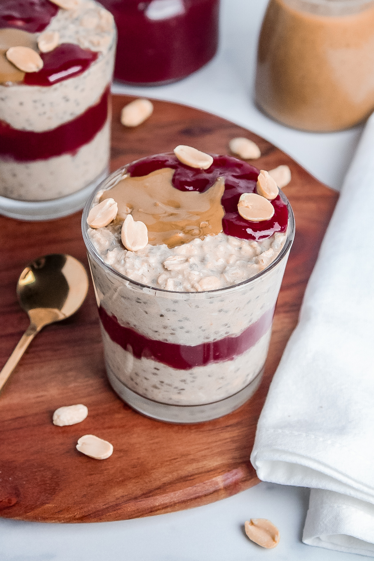 Peanut butter and jelly overnight oats in a glass, with a layer of raspberry jam in the middle and peanut butter, jam, and peanuts on top.
