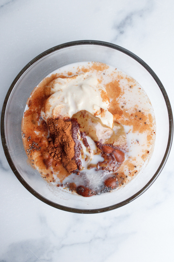Oats, non-dairy milk, non-dairy yogurt, peanut butter, maple syrup, chia seeds, vanilla, and salt combined in a bowl.