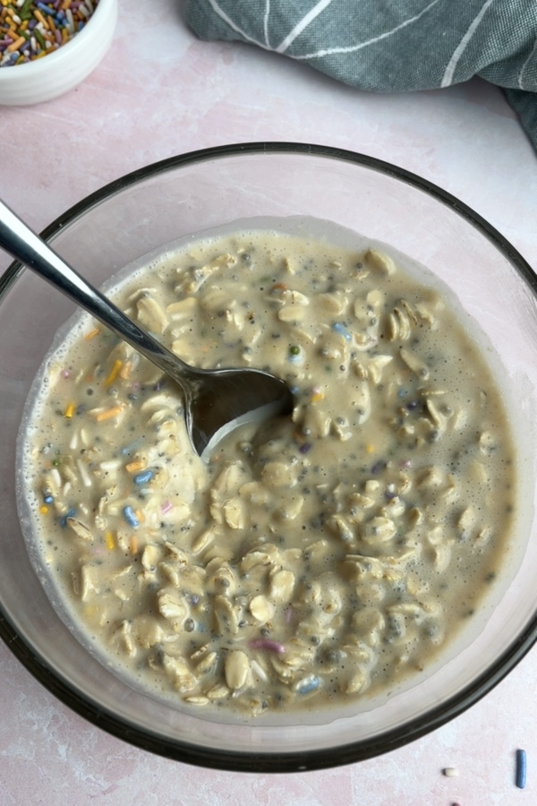 Birthday cake overnight oats mixture stirred together with a spoon, ready to be covered and soaked overnight.
