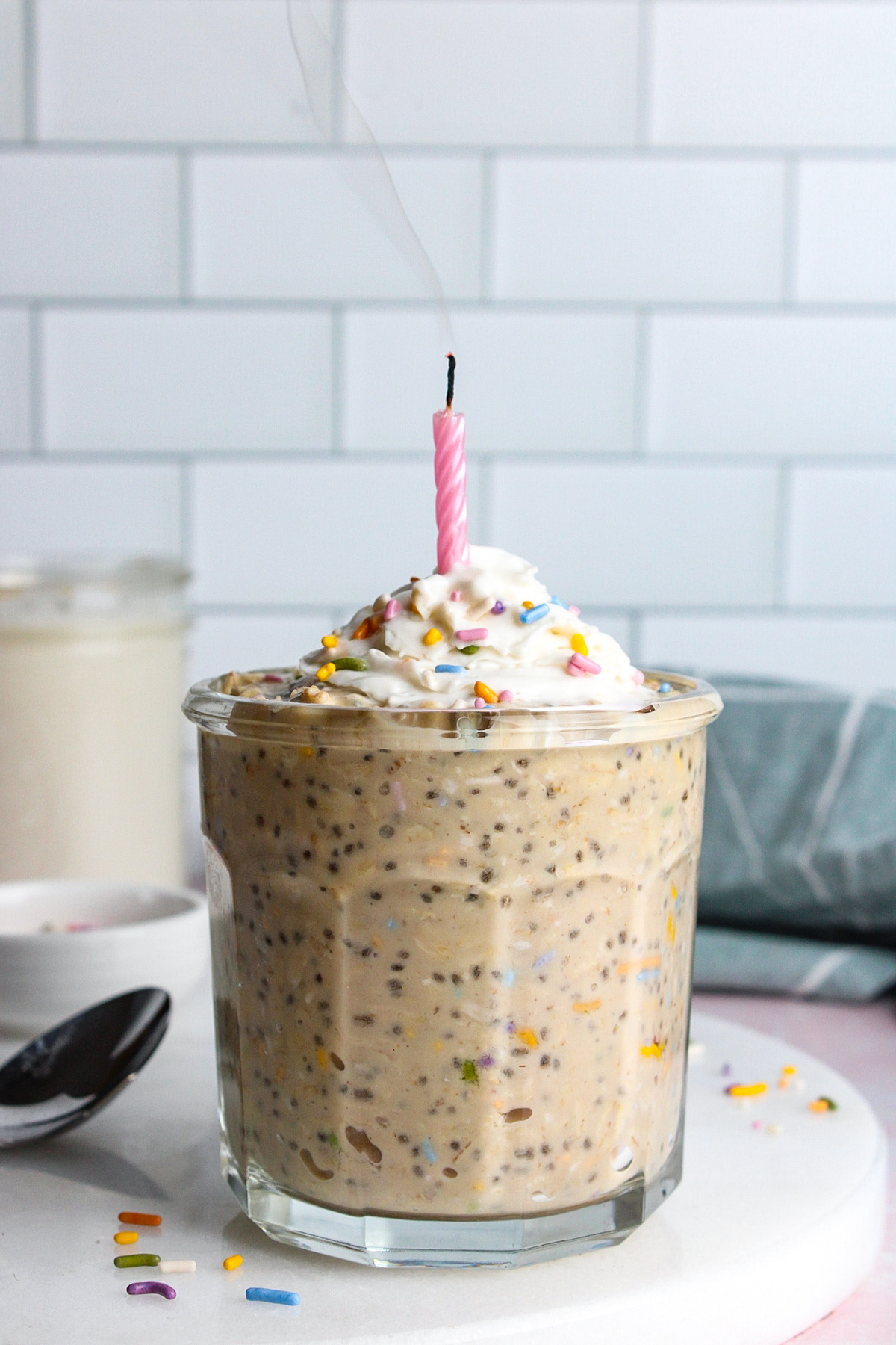Birthday cake overnight oats topped with whipped cream and sprinkles, with the candle just blown out.
