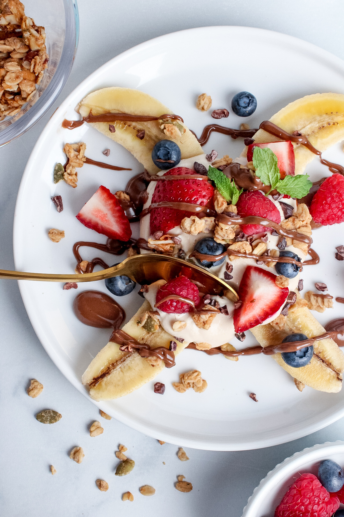 Overhead close-up of a vegan breakfast banana split, with a spoon taking a bite.