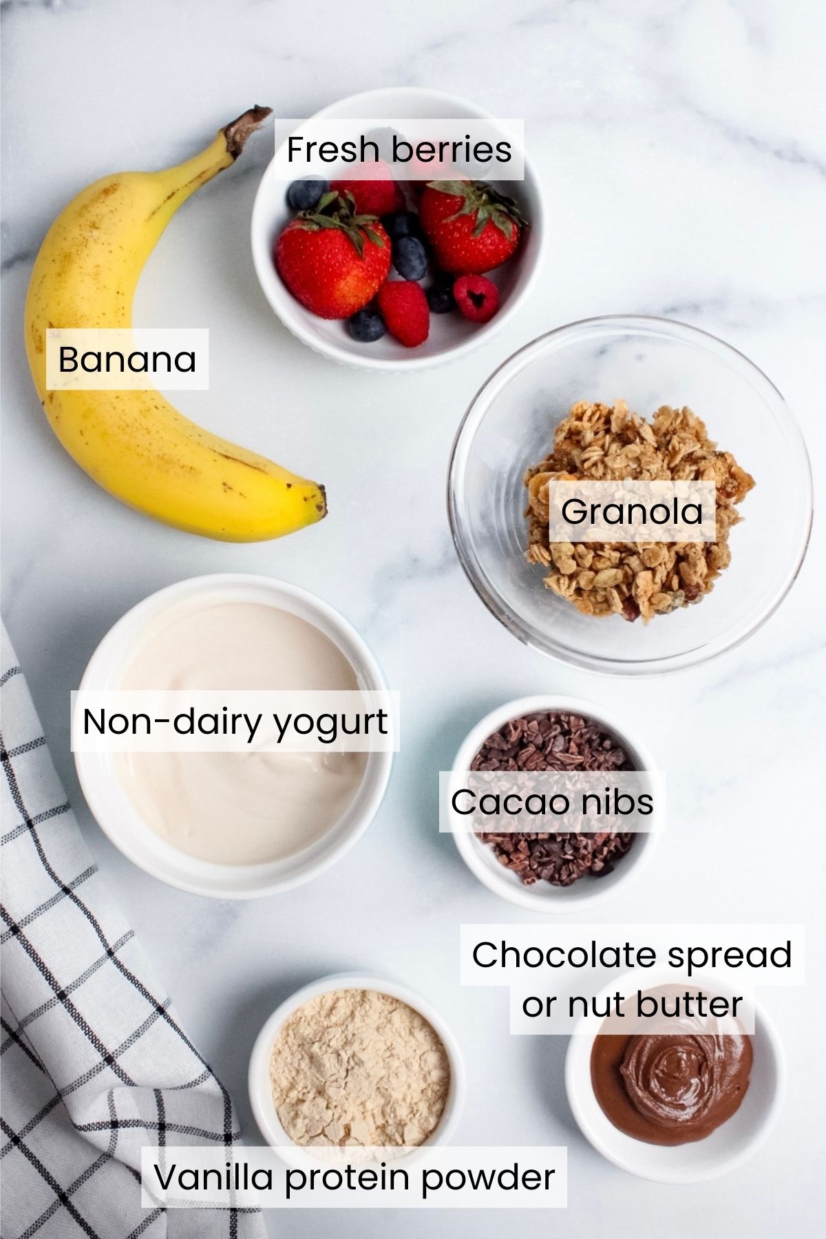 Ingredients for a breakfast banana split: banana, fresh berries, granola, non-dairy yogurt, cacao nibs, chocolate spread or nut butter, and vanilla protein powder.
