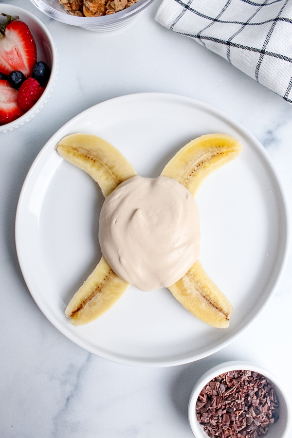 Banana halved lengthwise on a plate and topped with non-dairy yogurt.