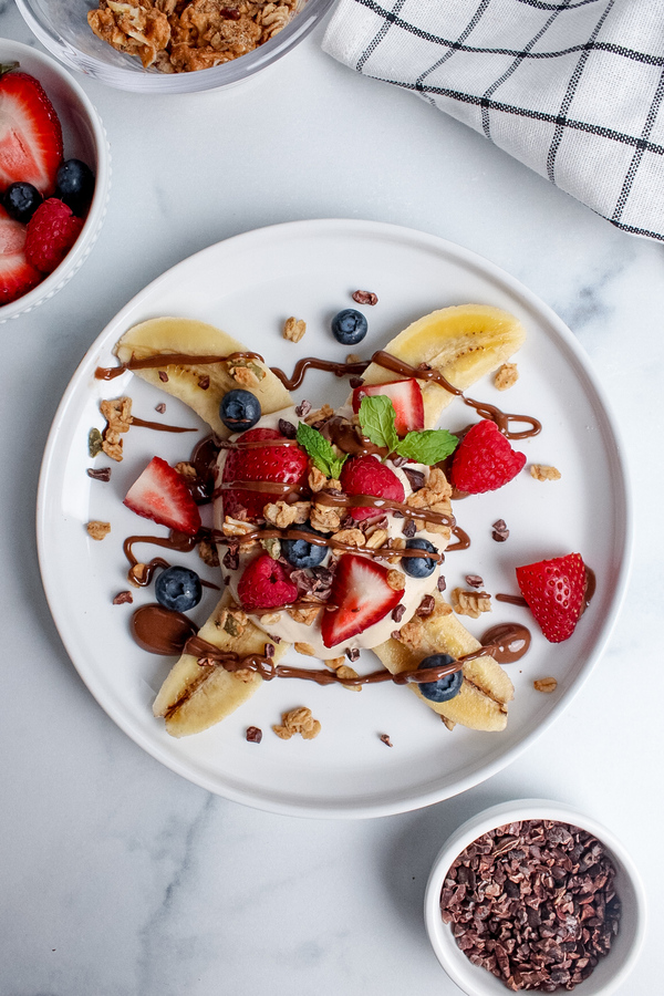 Adding fresh berries, granola, cacao nibs, and a drizzle of chocolate spread to a breakfast banana split.
