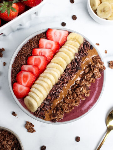 Strawberry banana espresso smoothie bowl topped with sliced strawberries, banana, granola, almond butter, and cacao nibs.