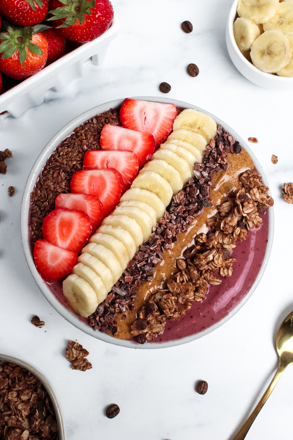 Strawberry banana espresso smoothie bowl topped with sliced strawberries, banana, granola, almond butter, and cacao nibs.